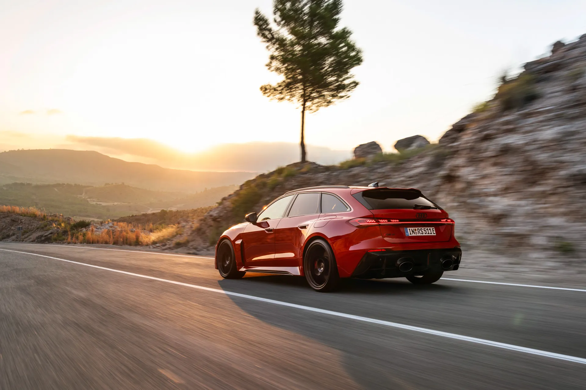 2027 Audi RS5 Avant driving on mountain road at sunset rear three quarter view