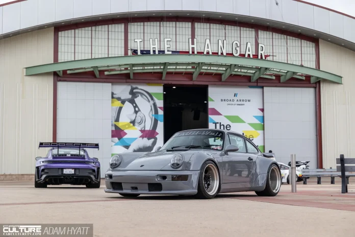 A slate gray Rauh-Welt Begriff 993-generation Porsche 911 parked in front of The Hangar building at the OC Fair & Event Center during Air | Water 2026, with a purple 992 GT3 RS visible in the background. Photo by Adam Hyatt for CarCultureTV.